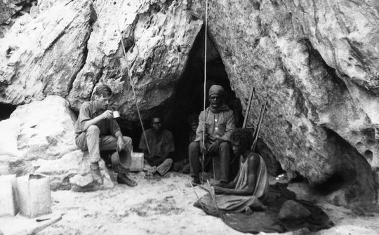 Felsnische am Bathurst Head (Thartali) auf der Cape York Halbinsel, die während der Expedition als Unterkunft diente. Im Bild: Norman Tindale von der Universität Adelaide und ortsansässige australische Ureinwohner. Fotografiert von Herbert Hale im Februar 1927.