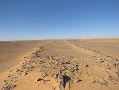 Blick entlang der Längsseite eines Mustatil-Baus. Die Forscher, die ganz klein am hinteren Rand der Struktur zu sehen sind, verdeutlichen dessen gewaltige Dimension. Das Bild zeigt die Struktur dieser Bauten als zwei Plattformen, die durch niedrige Wände verbunden sind.